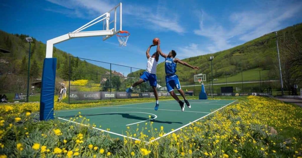 A basketball hoop on a scenic outdoor court, with players engaged in a dynamic game under a bright blue sky.