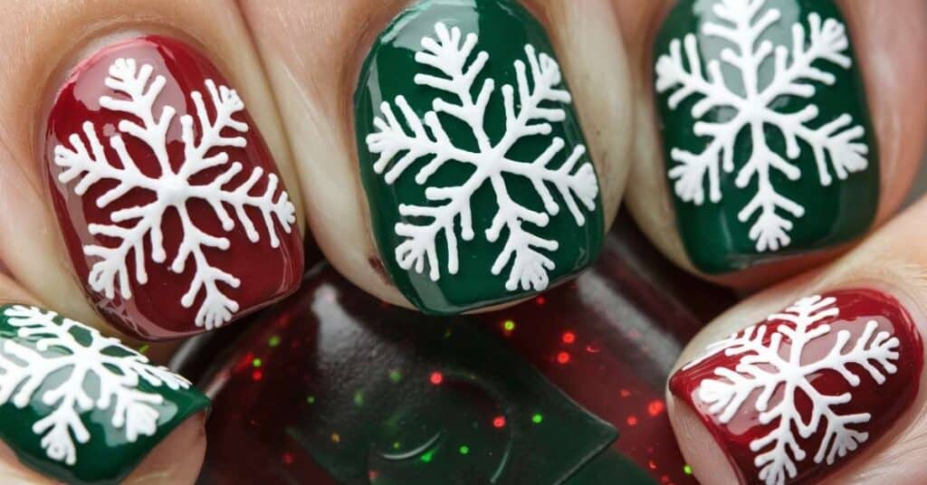 Detailed snowflake nail art with white snowflakes on red and green polish, showcasing a classic holiday design for Christmas nails.