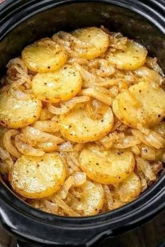 Sliced yellow potatoes and onions cooked with butter, garlic, and herbs in a black slow cooker.